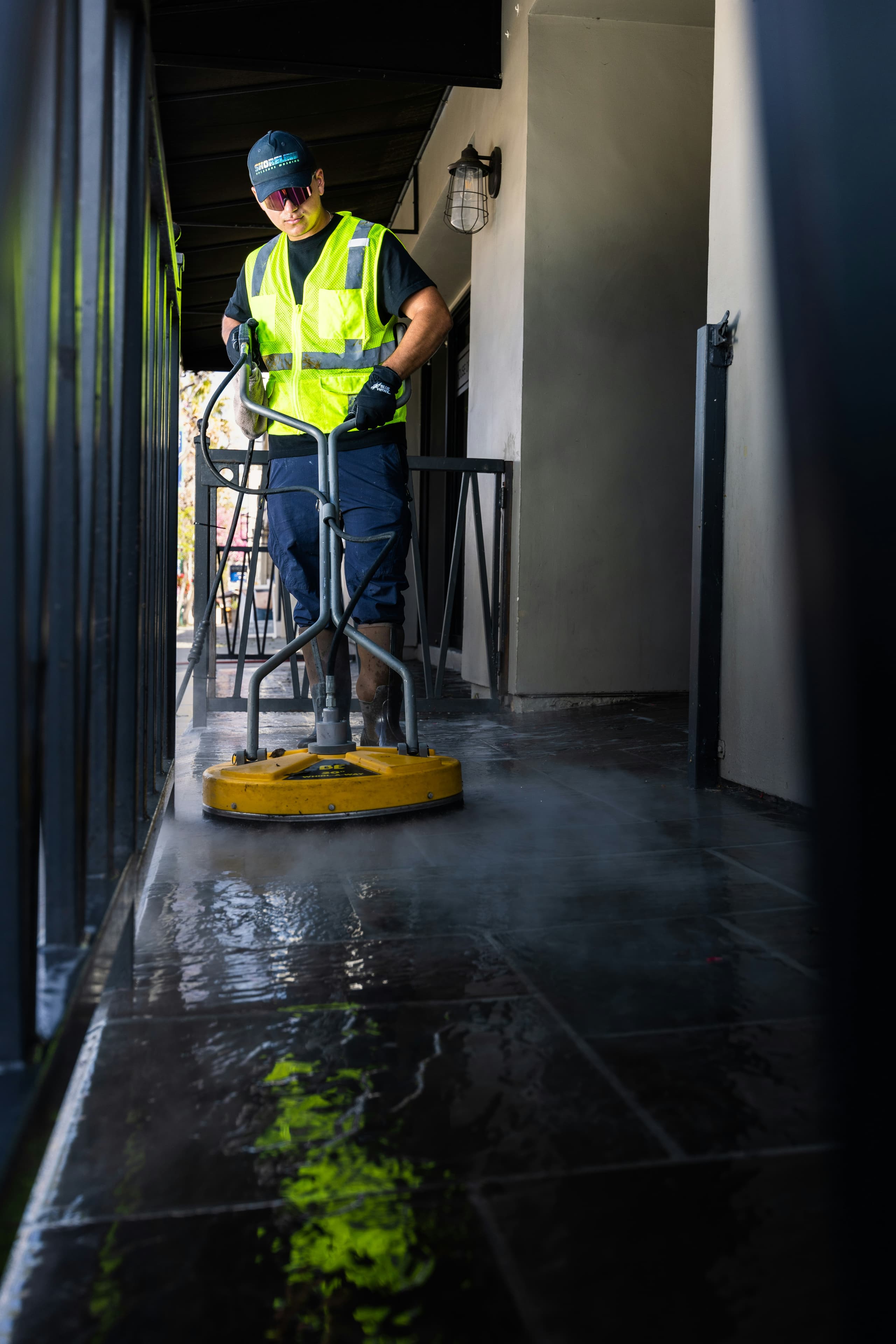 A cleaner in a hi-vis vest running a surface scrubber along a new-build walkway
